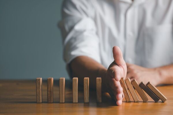 Hand stoppt fallende Dominosteine aus Holz – Symbol für Krisen-PR und Schadensbegrenzung
