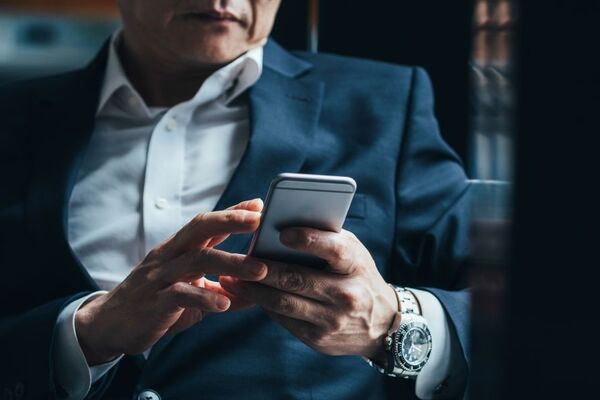 Person im Anzug liest Nachricht auf dem Smartphone – Symbolbild für Verleumdungskampagne und Rufmord