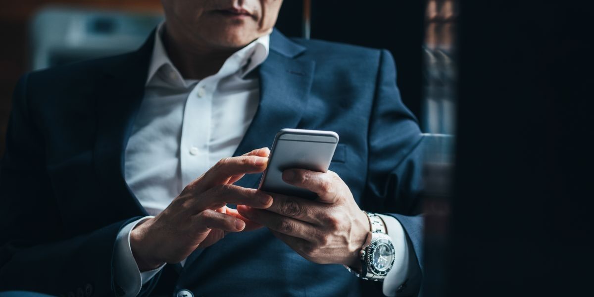 Person im Anzug liest Nachricht auf dem Smartphone – Symbolbild für Verleumdungskampagne und Rufmord